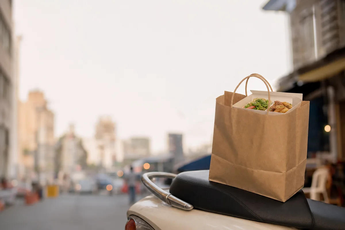 A takeout delivery bag with a boxed meal on a scooter seat