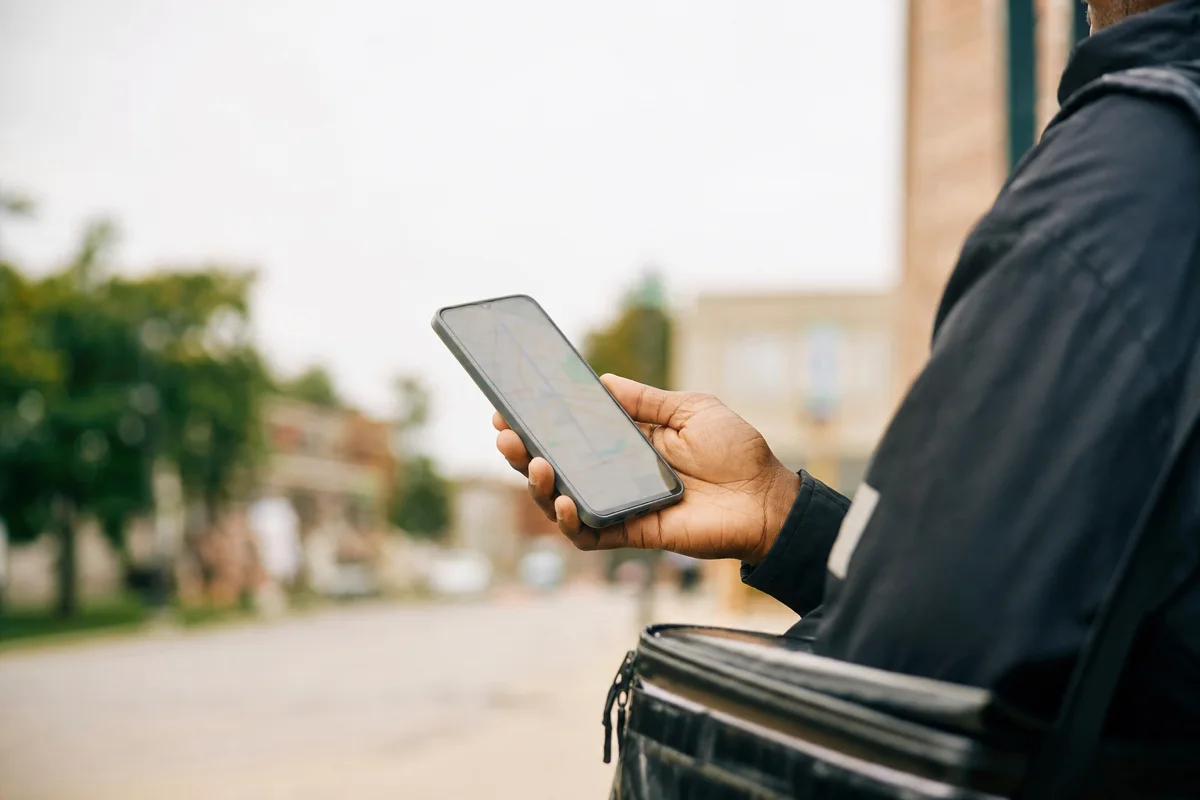 A delivery courier holding a phone with an insulated bag on their shoulder
