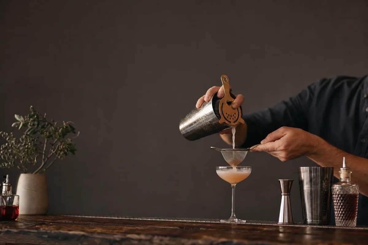 A bartender pouring a cocktail on a dark wood bar counter