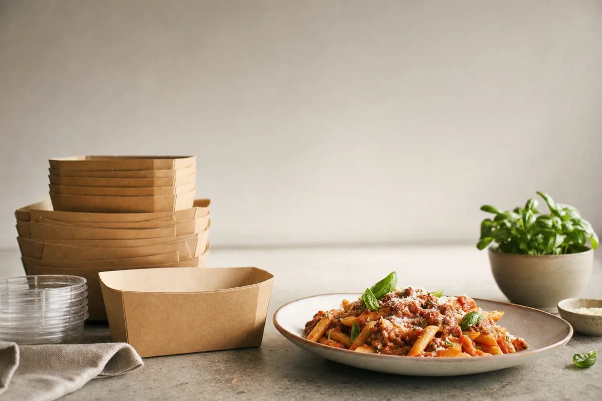 A stack of empty takeout containers beside a plated pasta dish