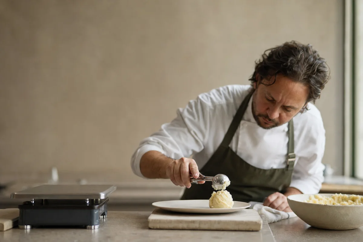A chef using a portion scoop to plate mashed potatoes beside a kitchen scale