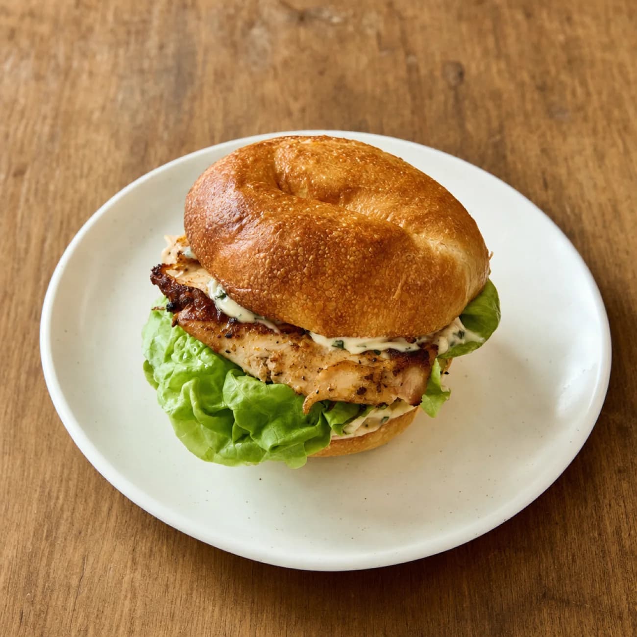 A grilled chicken sandwich with lettuce on a white plate, on a wooden table